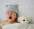 Newborn yawning from tiredness while lying in bed with a soft toy